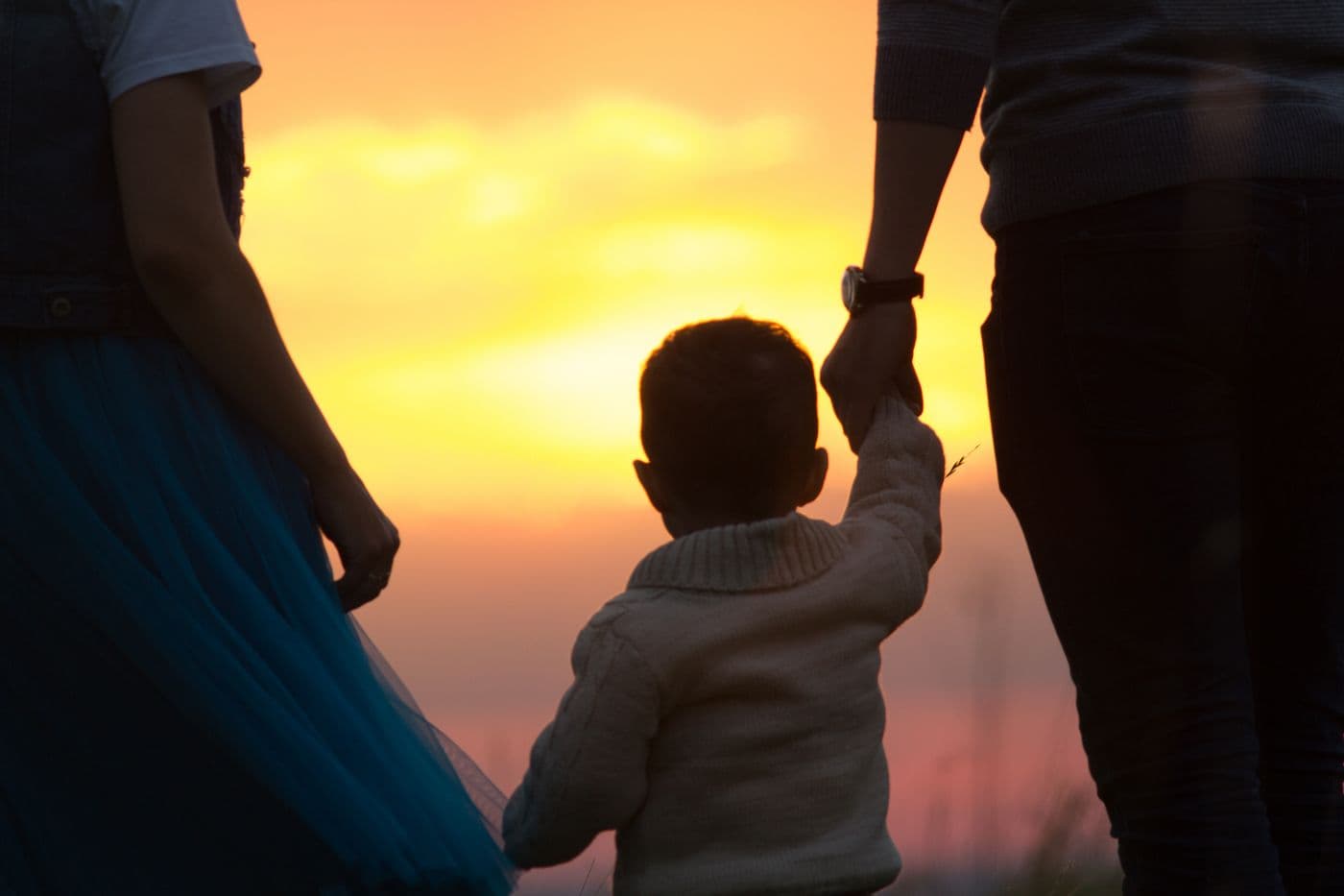 Sunset boy holding hands with parents